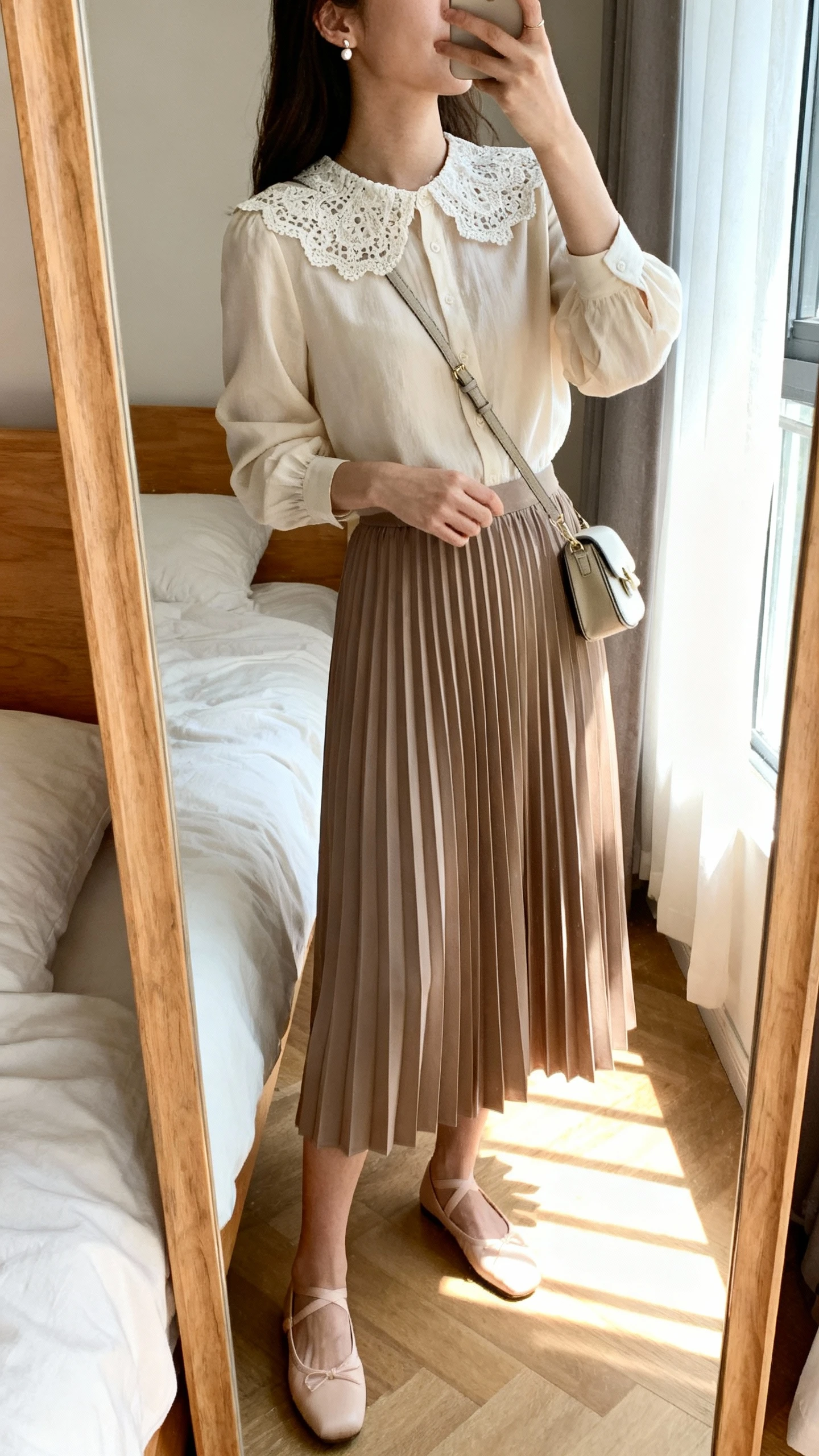 iPhone side-angle mirror selfie of a woman wearing a lace-collar blouse with a knee-length pleated skirt, ballet flats, delicate stud earrings, and a small crossbody, face not visible, cropped at shoulders, bedroom mirror, natural window light, iPhone photo quality.