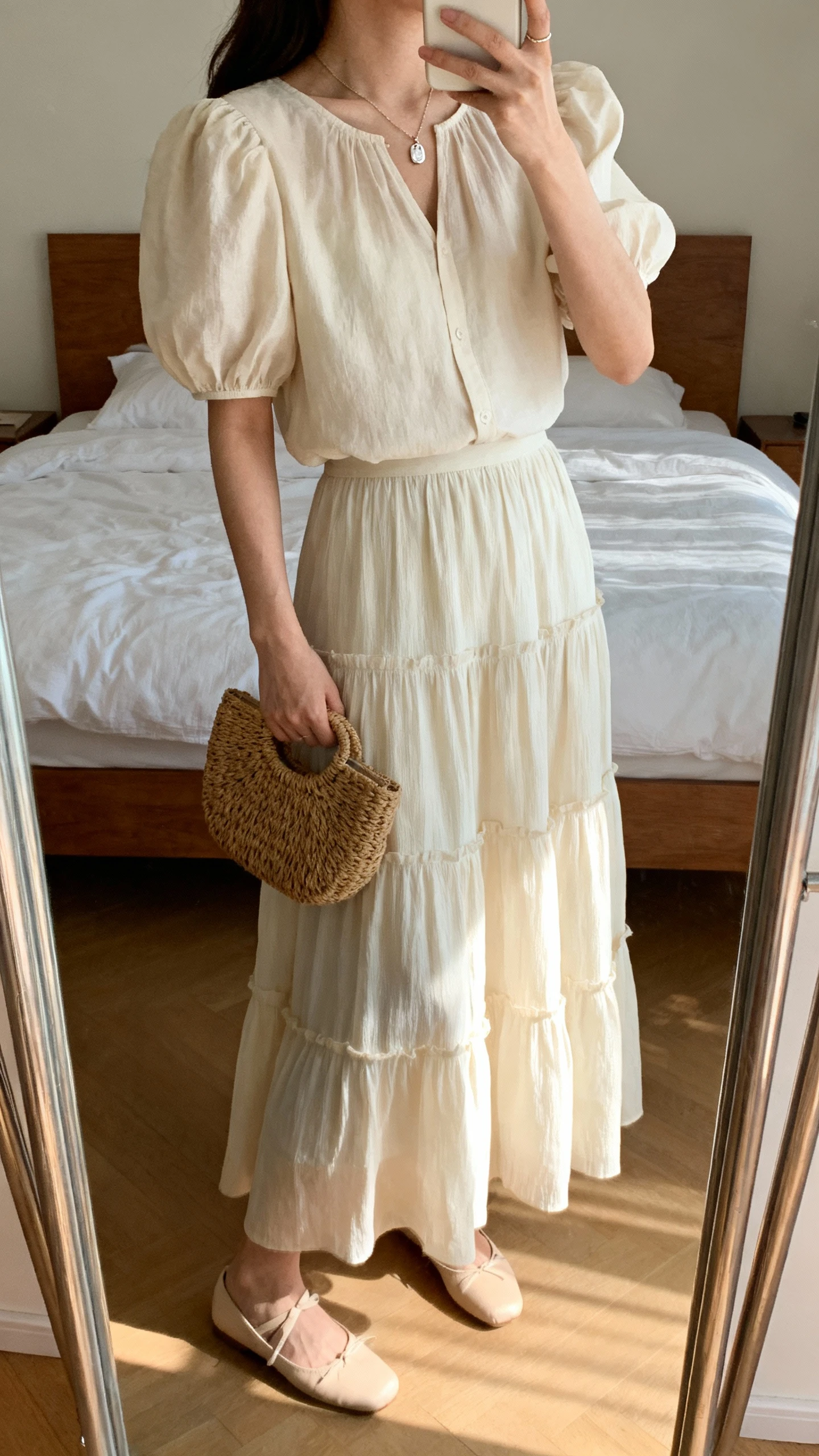 iPhone side-angle mirror selfie of a woman wearing a romantic puff-sleeve blouse with a tiered maxi skirt, dainty pendant necklace, ballet flats, and a woven clutch, face not visible, cropped at shoulders, bedroom mirror, natural daylight, iPhone photo quality.