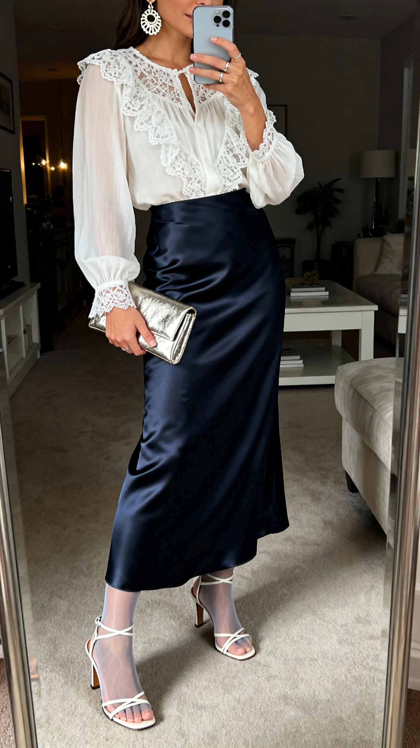 iPhone side-angle mirror selfie of a woman wearing a bias-cut satin maxi skirt in midnight with a lace-trim blouse, strappy mid-heel sandals, a metallic clutch, statement earrings, and a delicate ring; optional sheer hosiery implied, face not visible, living room full-length mirror, evening indoor lighting, iPhone photo quality.