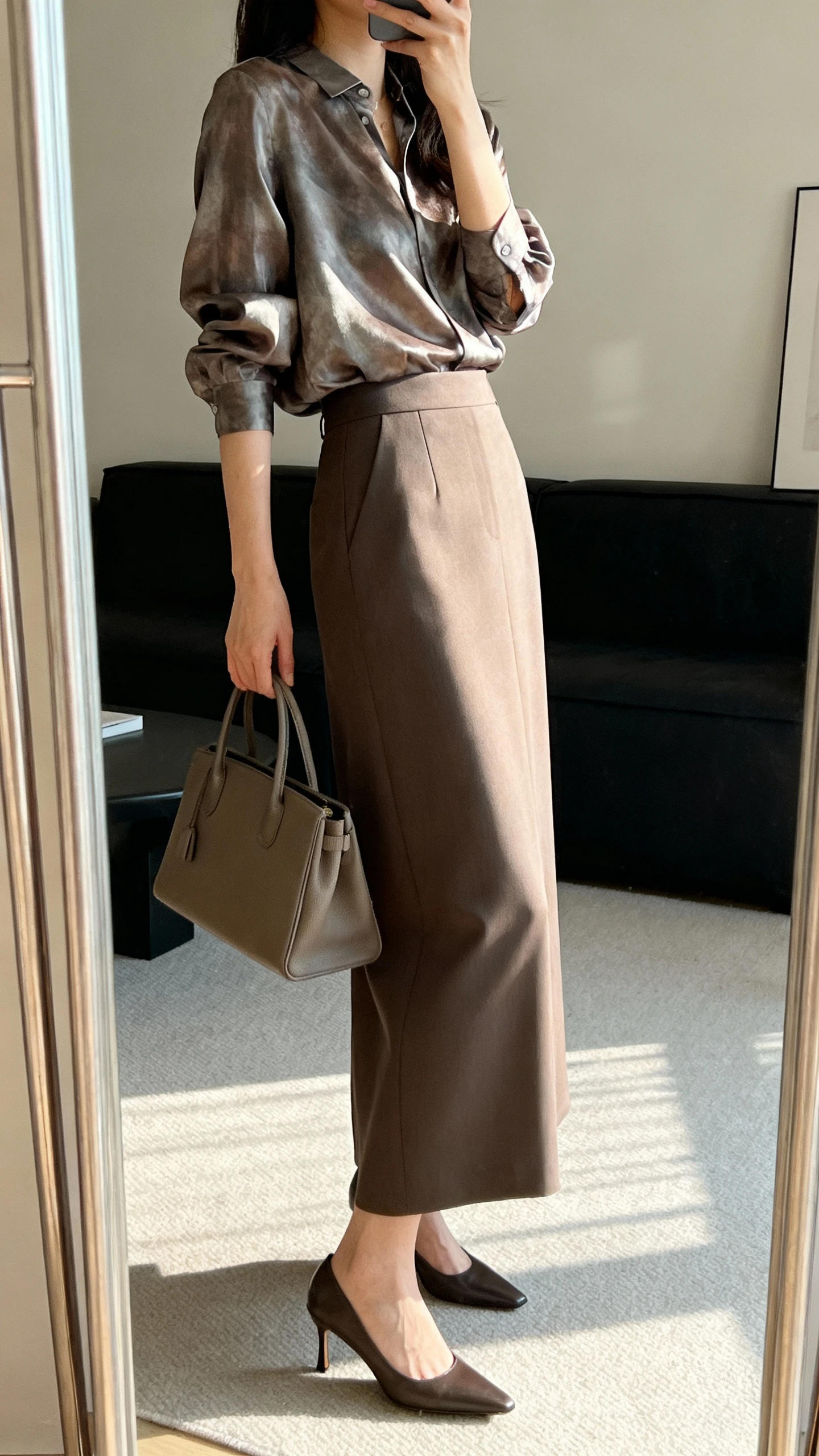 iPhone side-angle mirror selfie of a woman wearing a silk-blend blouse with a tailored maxi skirt for elegant minimalist chic, styled with a structured tote and sleek low heels, face not visible, living room full-length mirror, soft afternoon light, iPhone photo quality.