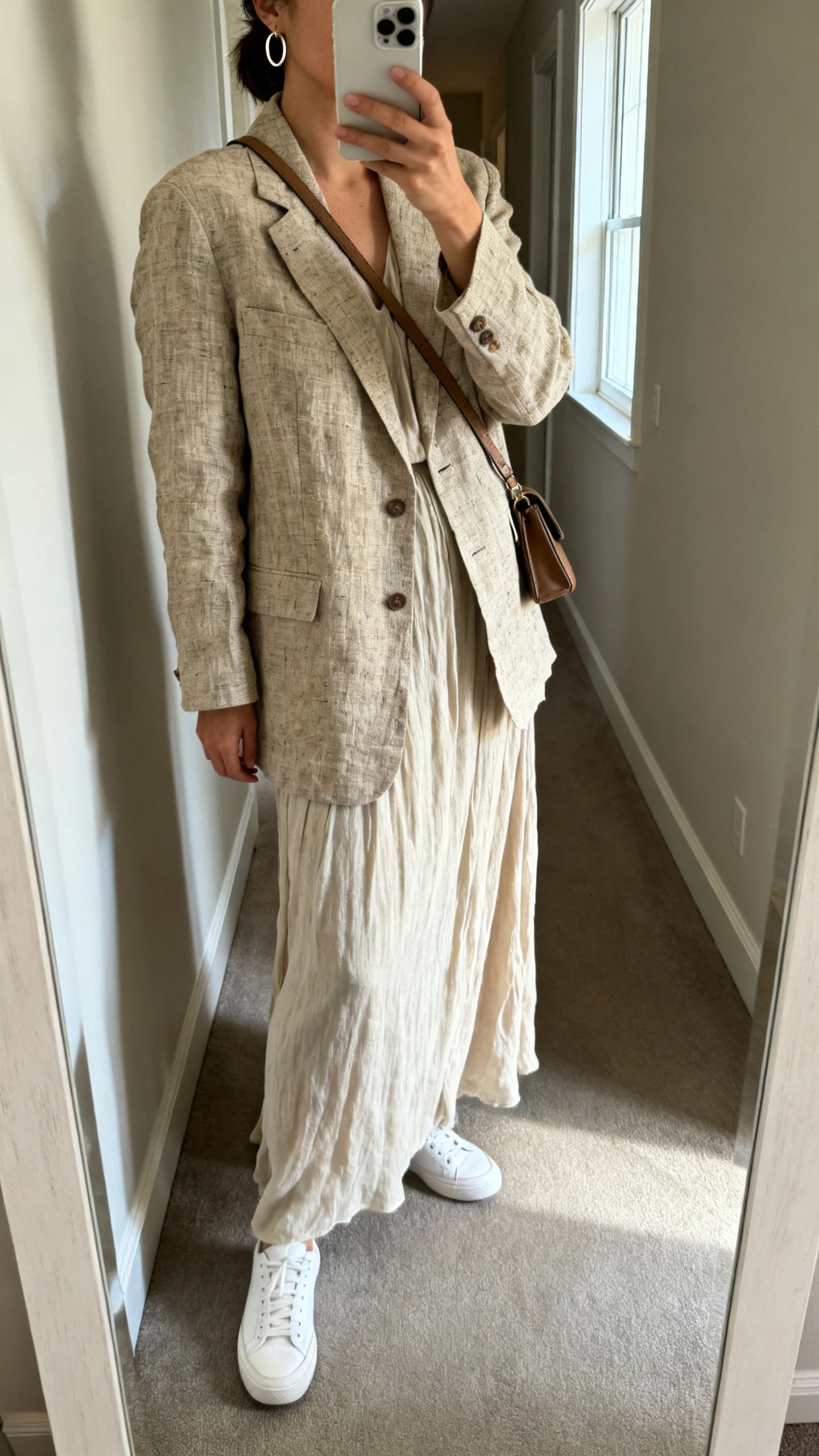 iPhone side-angle mirror selfie of a woman wearing a linen blazer over a flowy maxi dress with low-key white sneakers and a crossbody bag, subtle hoop earrings, face not visible, hallway full-length mirror, natural window light, iPhone photo quality.